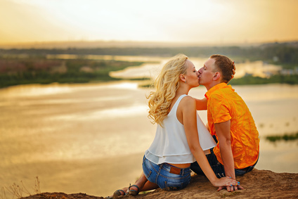 Loving couple sitting on the river bank. Kiss. Sunset. Summer day. The concept of a romantic relationship.